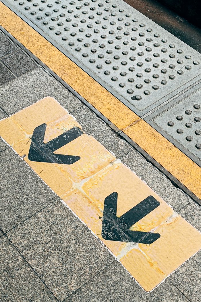 services-01 View of urban sidewalk with black directional arrows on yellow pavement indicating pedestrian direction.