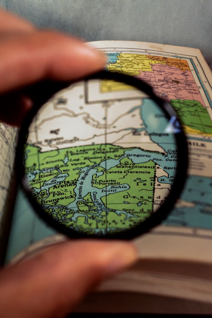 gallery-5 Close-up view of a hand holding a magnifying glass over a colorful map, enhancing details.