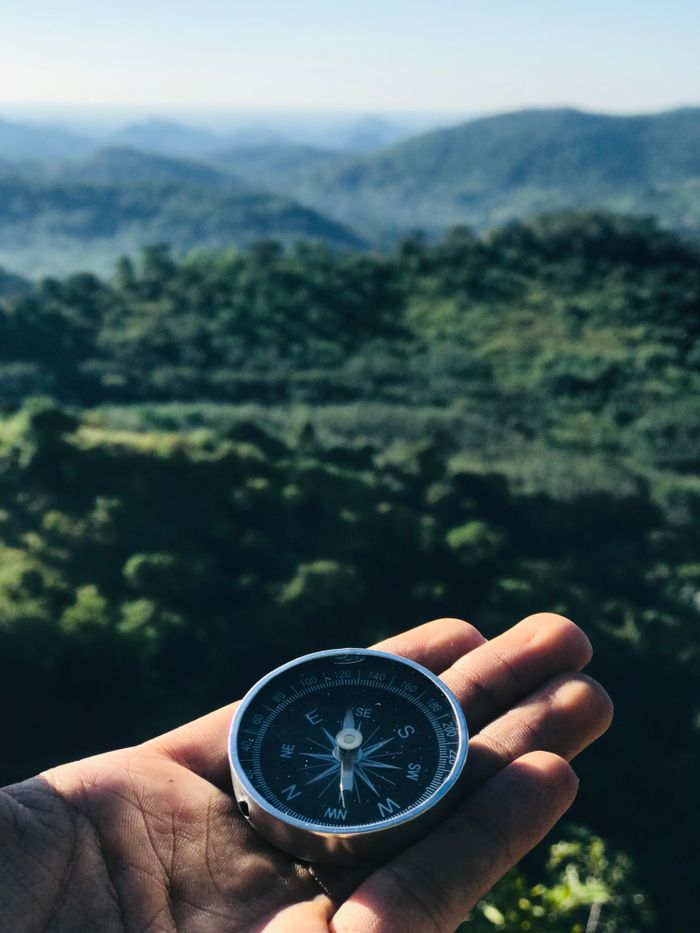 services-02 A handheld compass over majestic green mountains under blue skies, ideal for travel themes.