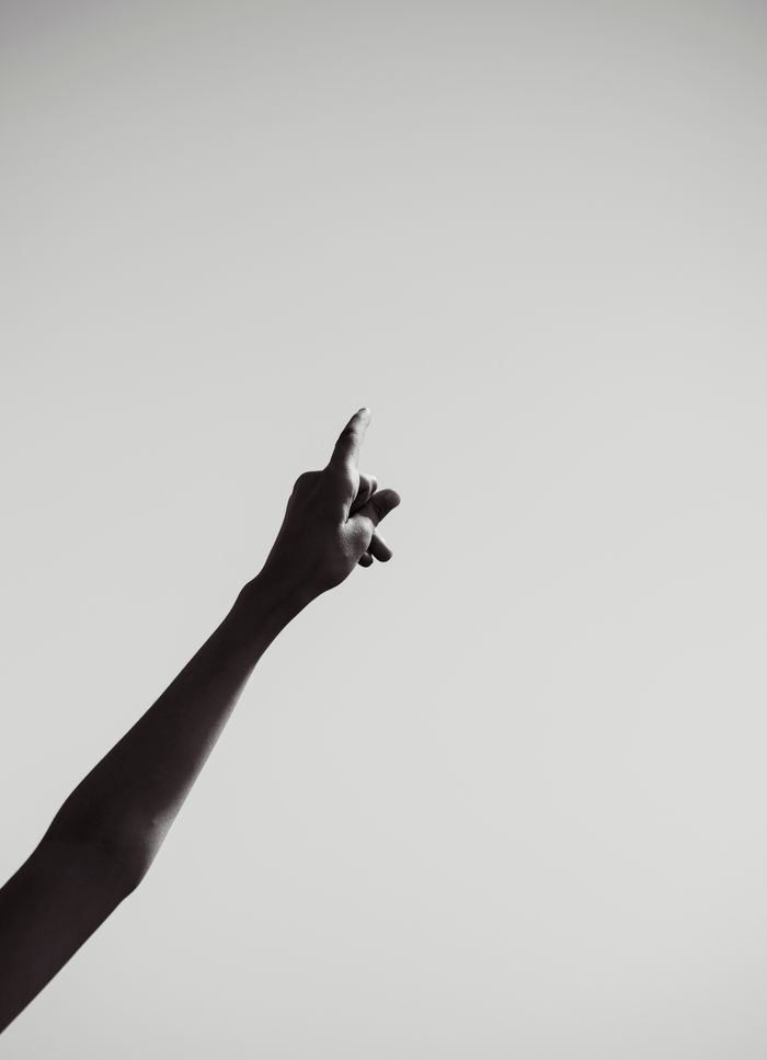 services-03 A black and white silhouette of a raised arm with a pointing finger against a blank background.
