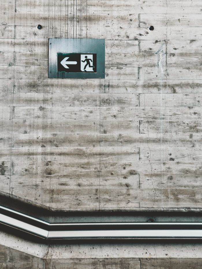 about-img Industrial concrete wall with an emergency exit sign and pipes, highlighting urban design.