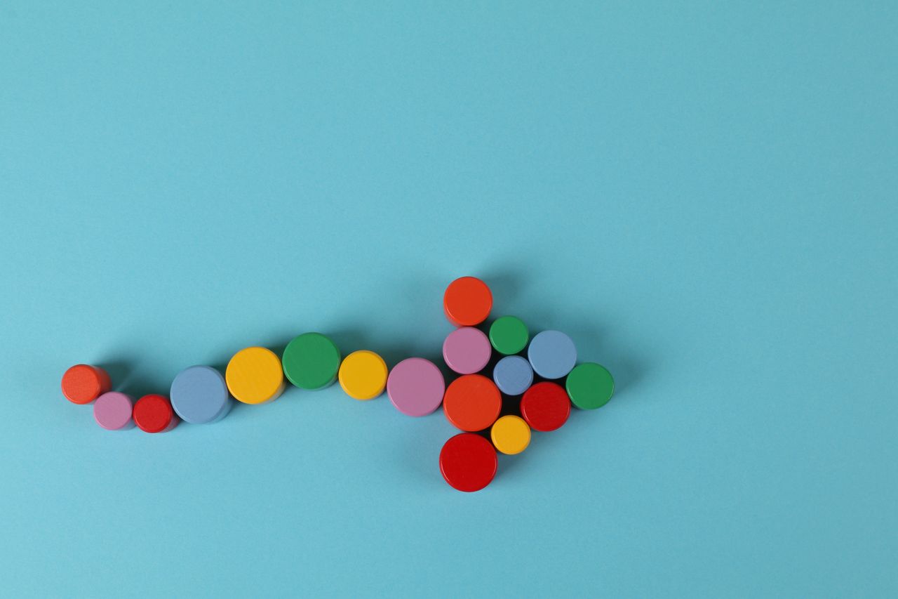 services-01 A vibrant arrow composed of colorful cylinders against a minimalist blue backdrop.